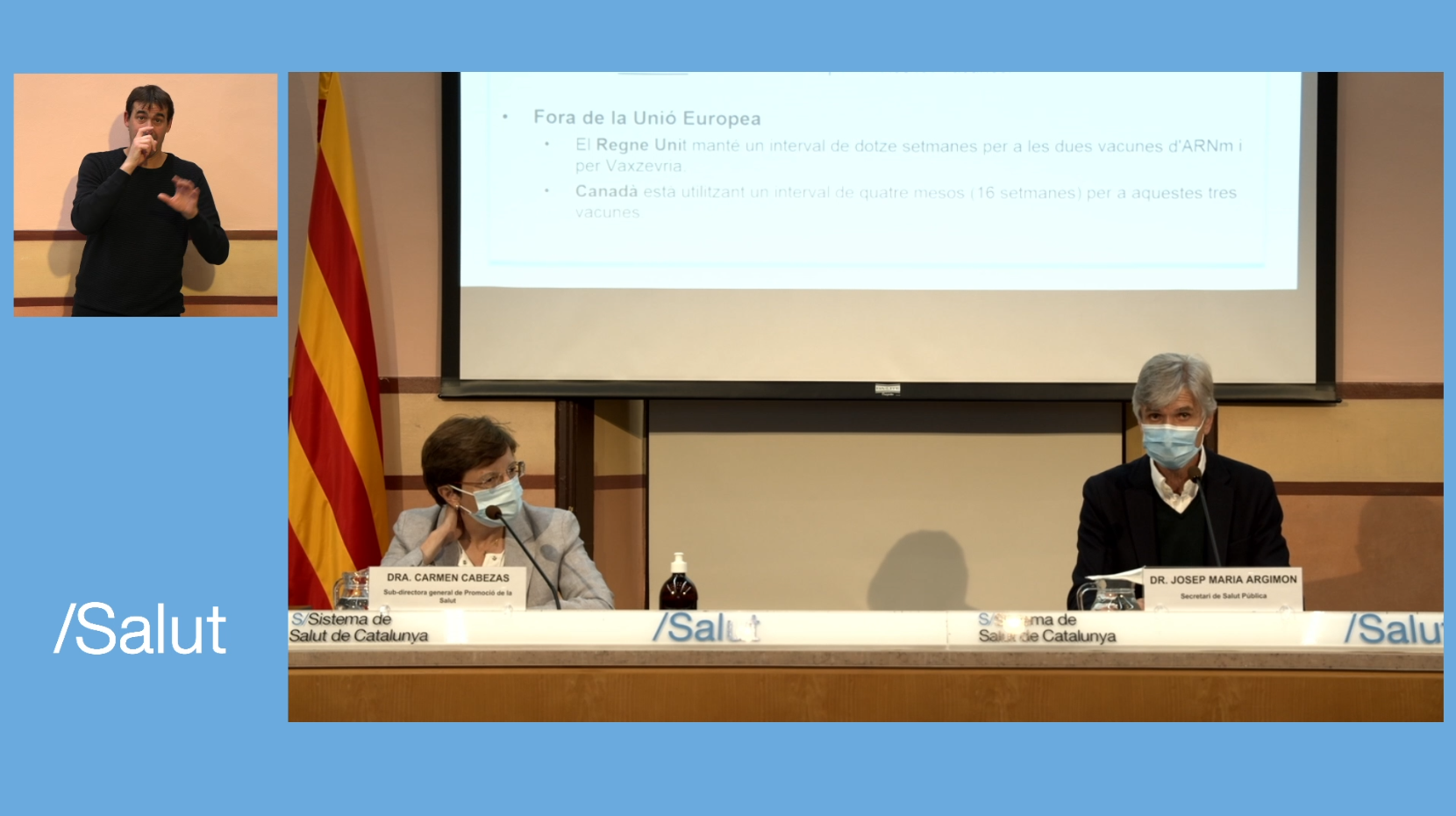 Taula rodona institucional del Departament de Salut de Catalunya amb dues persones ponents assegudes darrere una taula, una pantalla de projecció al fons i un intèrpret de llengua de signes catalana en una finestra lateral.