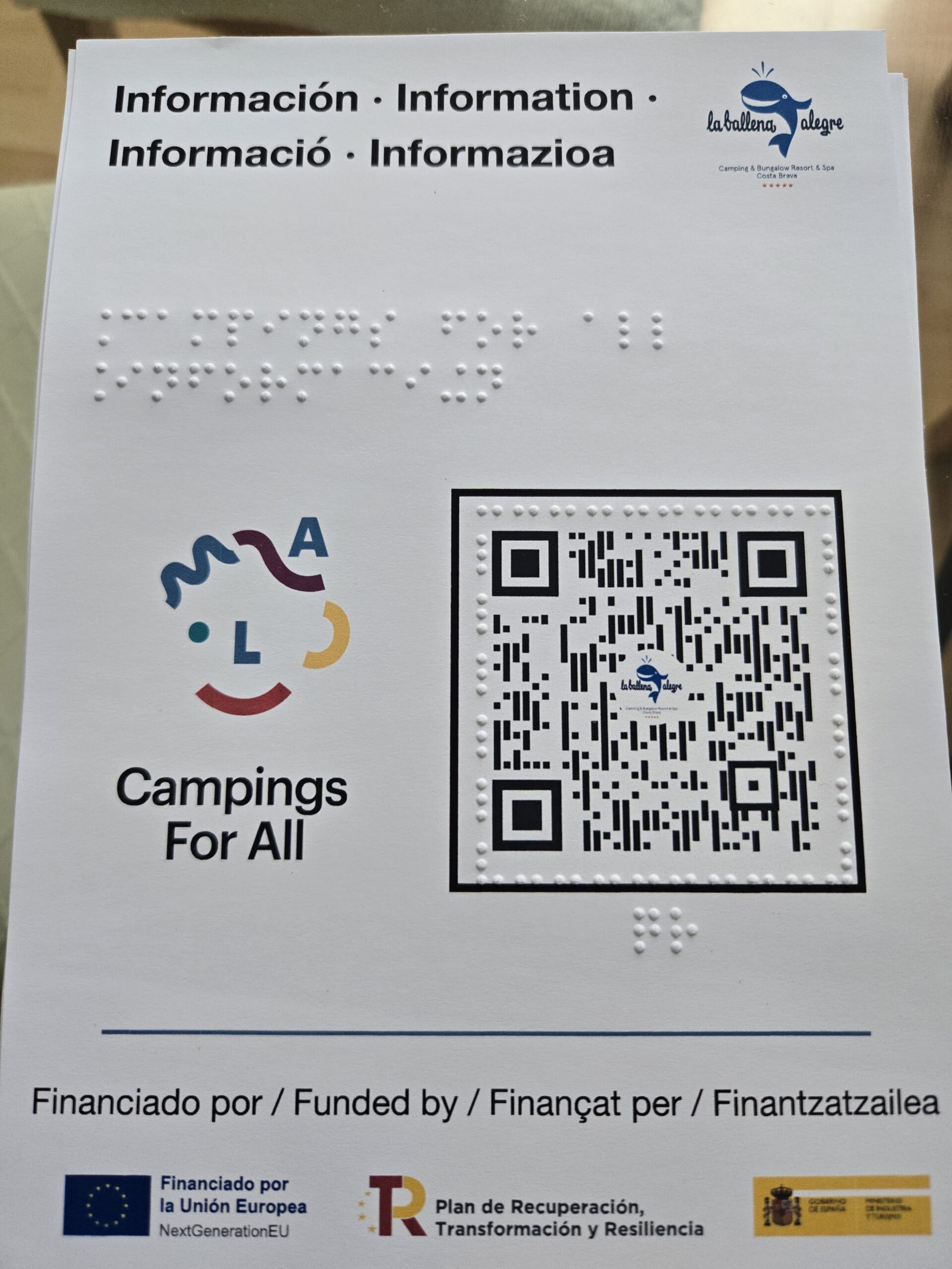 Fitxa informativa en blanc amb text en espanyol, anglès, català i euskera. Conté escriptura braille en relleu, el logotip de Campings For All, un codi QR i els logotips de finançament de la Unió Europea i el Pla de Recuperació.