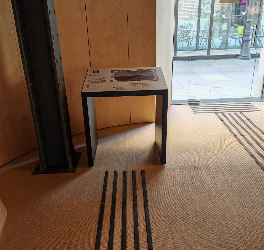 plafó informatiu tàctil situat a l'entrada d'un espai, amb bandes de paviment podotàctil que hi condueixen des de la porta.